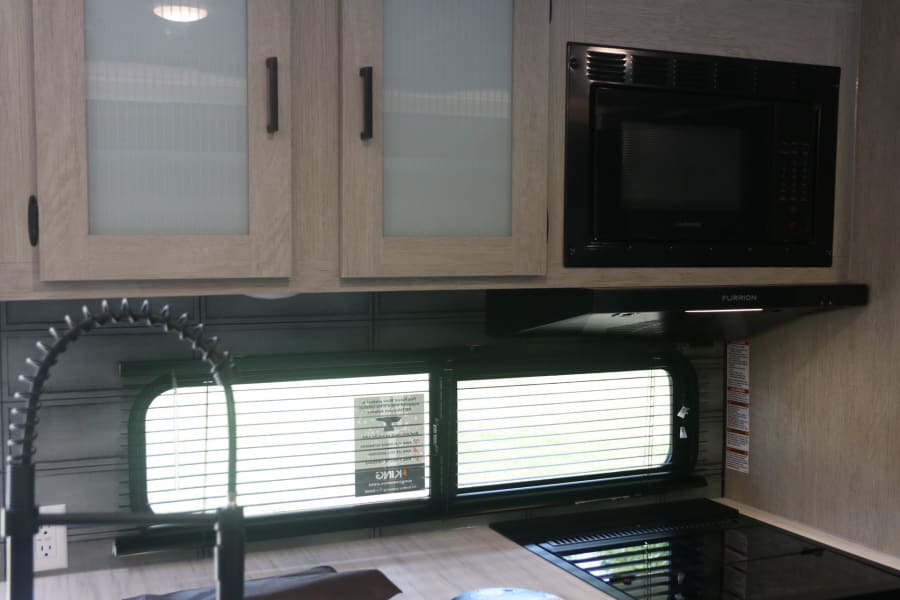 Compact RV rental kitchen with light wood cabinets, Furrion microwave, and cooktop. Includes sink with pull-down faucet.