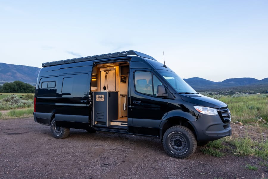 Explore the outdoors in this black custom Sprinter RV rental, featuring an open interior with kitchen and shower.