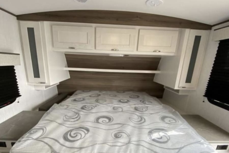 Spacious RV rental bedroom features a comfortable bed, ample overhead storage, and side cabinets, ideal for your travels.