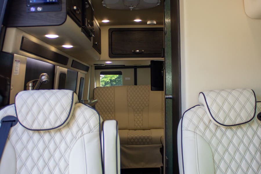 Step into a luxurious RV rental interior. Plush white quilted seats, modern kitchen, and smart controls await your journey.