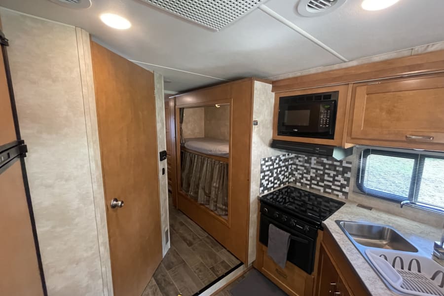 Explore this well-equipped RV rental kitchen with microwave, stove, sink, and adjacent bunk beds for comfortable travel.