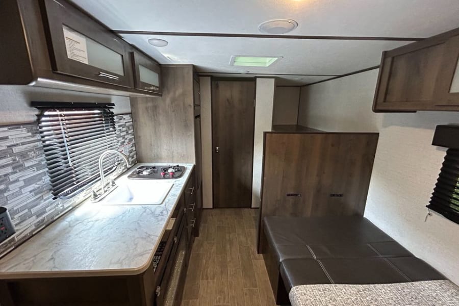 Inside a clean rv rental, view of a galley kitchen with sink/stove & ample counter space, plus a versatile bunk bed area.