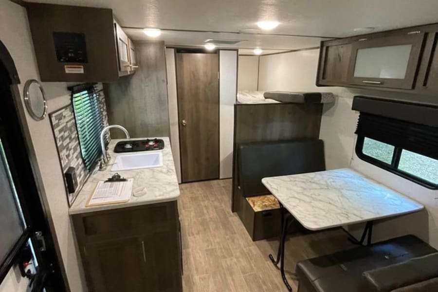 Modern rv rental interior with kitchen (left, sink, stove), dining booth, and bunk beds (rear). Comfortable travel space.