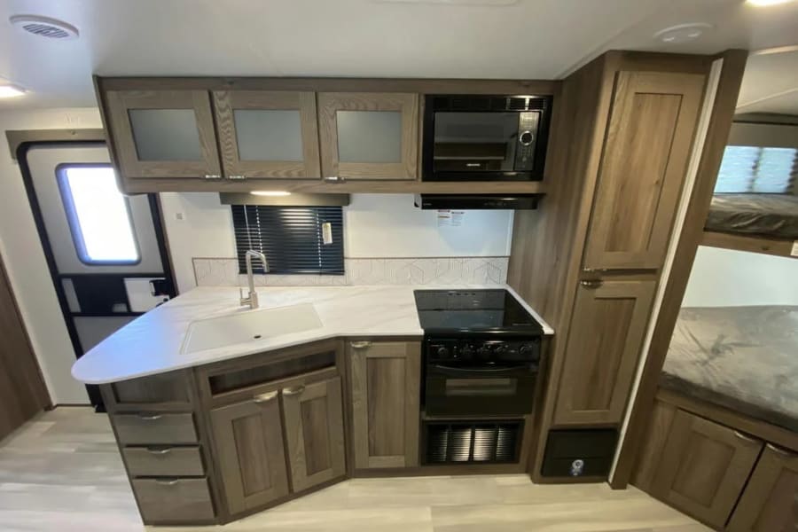 Spacious RV rental interior with modern kitchen, microwave, range, sink, and bunk beds. Perfect for family adventures.