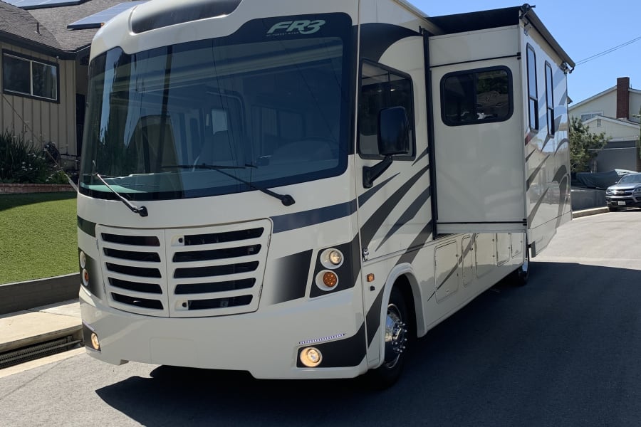 White FR3 motorhome with extended slide-out on a residential street, ready for your RV rental adventure.