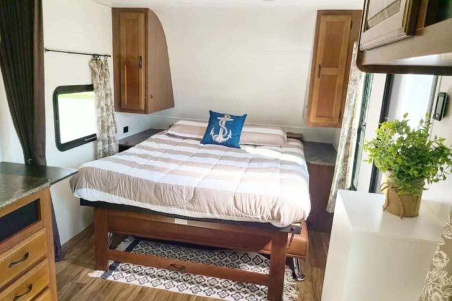 Cozy RV rental bedroom with striped bedding, an anchor pillow, wood cabinets, and a bright interior. Ideal for your next trip!