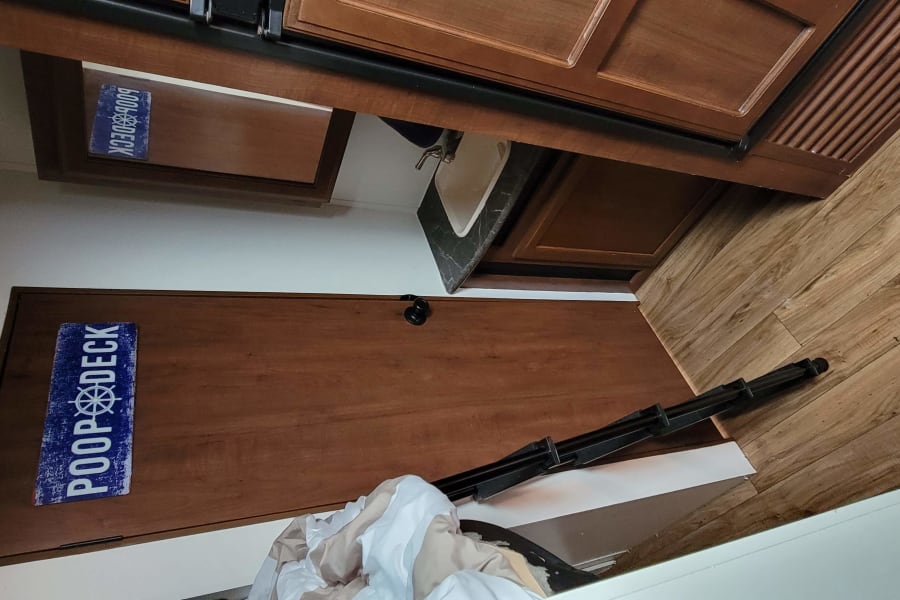 RV rental interior featuring wood floor, kitchen area with sink & cabinets, and a whimsical "POOP DECK" door sign.