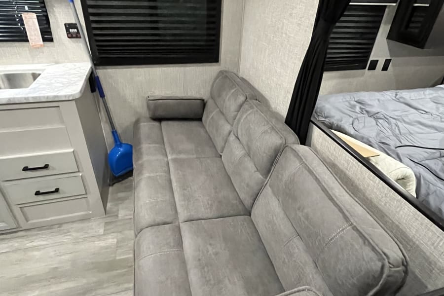 Inside an rv rental: a gray sofa, kitchen counter with sink, and a bed behind curtains. Designed for comfortable travel.