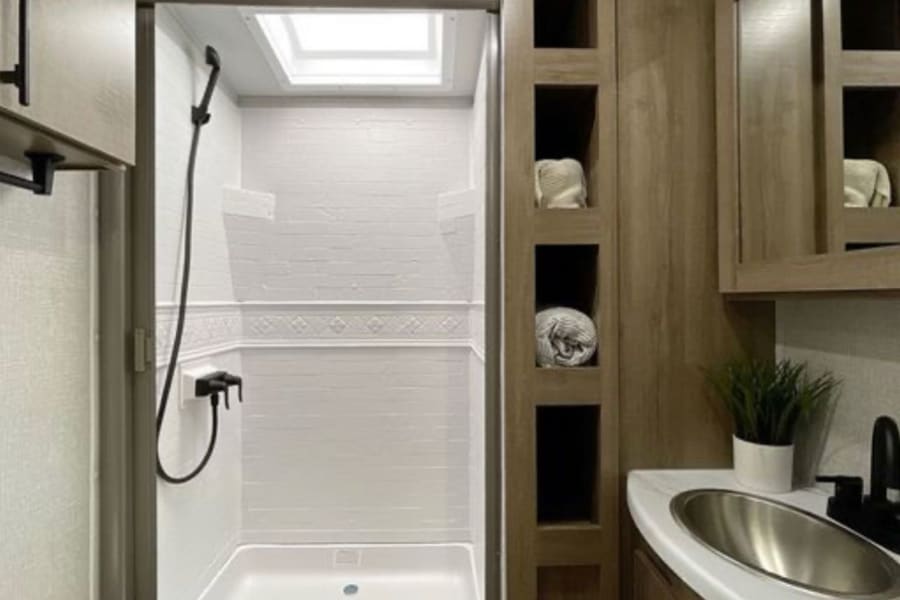 Clean RV rental bathroom showcasing a compact shower with skylight and a modern wood-look vanity with sink.