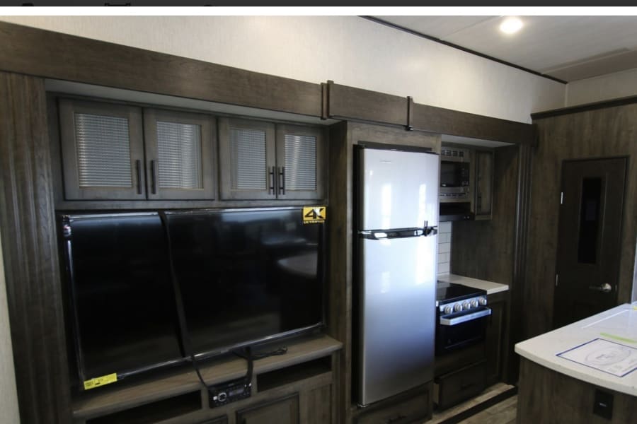Spacious rv rental interior featuring a modern kitchen with fridge/stove, TV entertainment area, and stylish dark wood cabinetry.