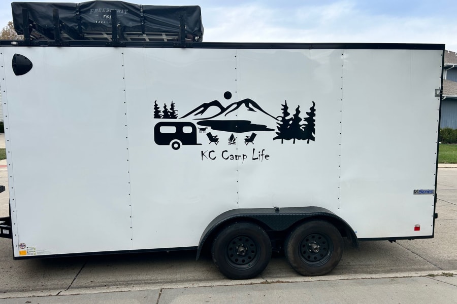 White enclosed trailer featuring a scenic camping graphic and rooftop tent, perfect for your next RV rental.