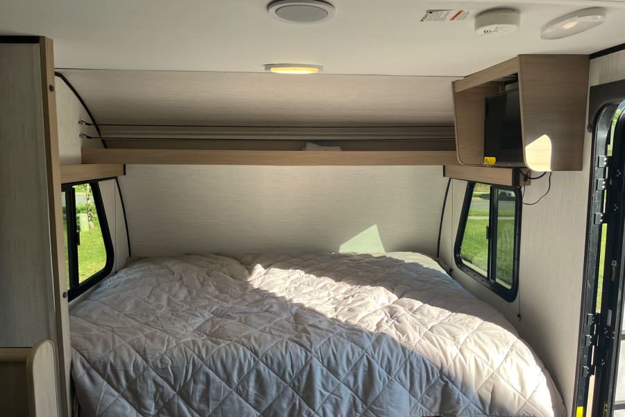 An RV rental bedroom showcasing a quilted bed, sunlight through windows, and a mounted TV. Perfect for travel.