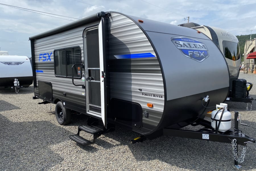 A gray and black Salem FSX travel trailer is parked on a gravel lot, door open. Ideal for your next RV rental.