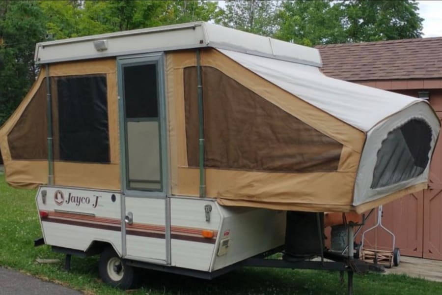 This tan and white pop-up camper, seen fully set up, is available for RV rental. Ideal for camping adventures.