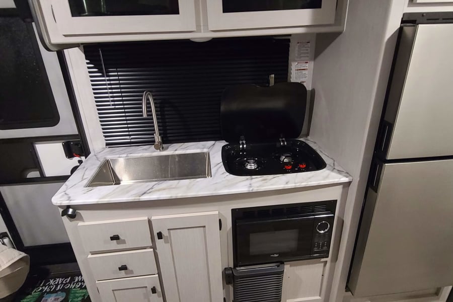Compact RV rental kitchen features a sink, two-burner stove, microwave, and refrigerator for your travels.