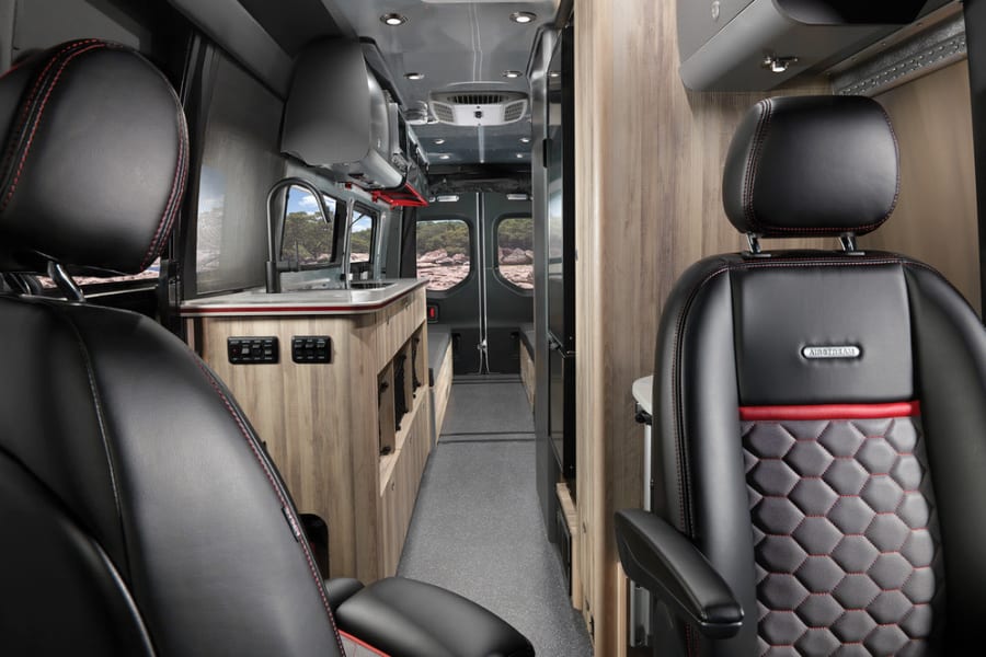 Airstream RV rental interior showing luxury black leather seats, red accents, and a modern galley kitchen.