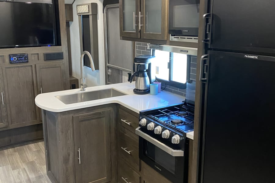Spacious RV rental interior featuring a modern kitchen with island sink, stove, fridge, and TV. Ideal for travels.