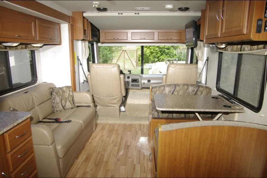 Spacious rv rental interior featuring a cozy living area, dinette, kitchenette, and driver's cabin. Ideal for road trips.