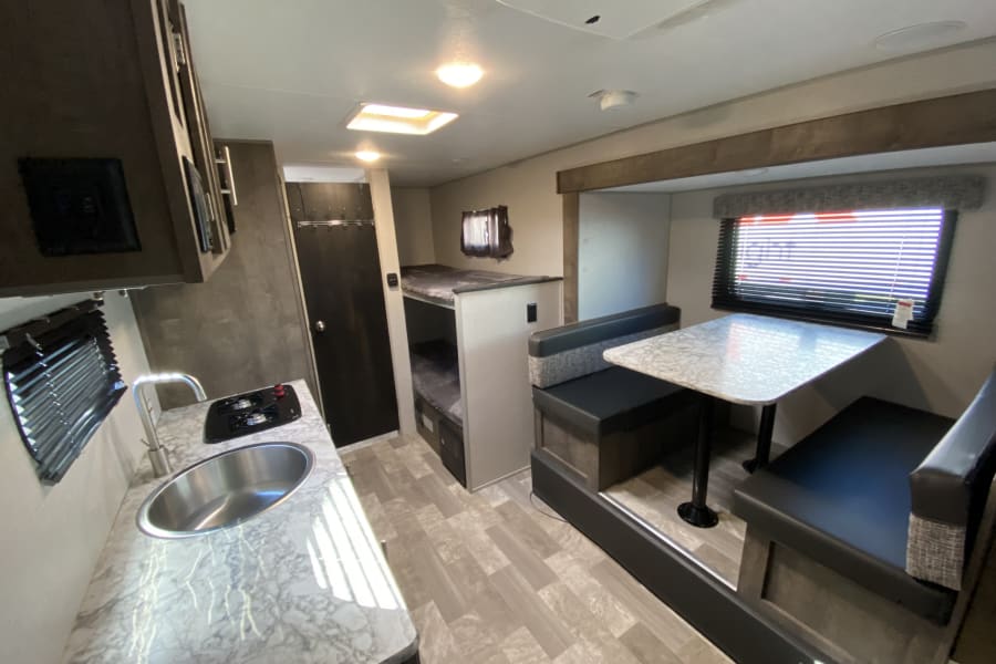 This RV rental interior features a kitchen with sink and stovetop, a cozy dinette, and convenient bunk beds for comfortable travel.
