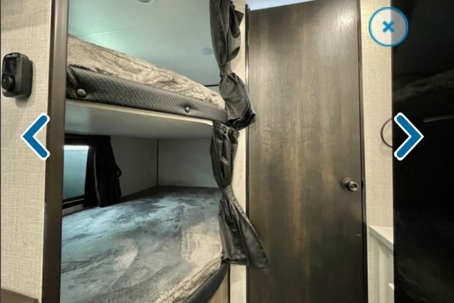 RV rental interior showing comfortable bunk beds with privacy curtains, a ceiling vent, and a closed wooden door.