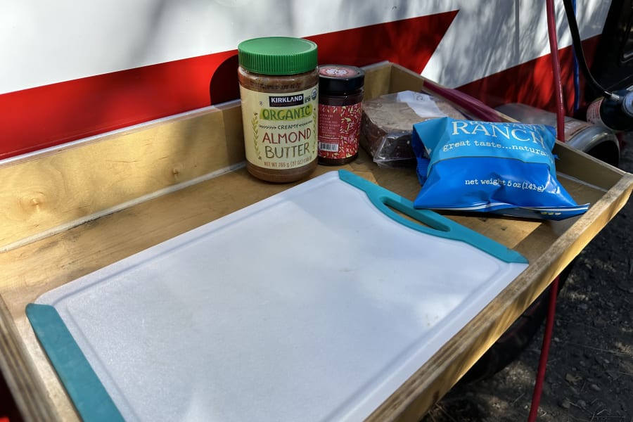 Preparing snacks on an RV rental pull-out tray: almond butter, jam, chips, and a cutting board for easy camping meals.