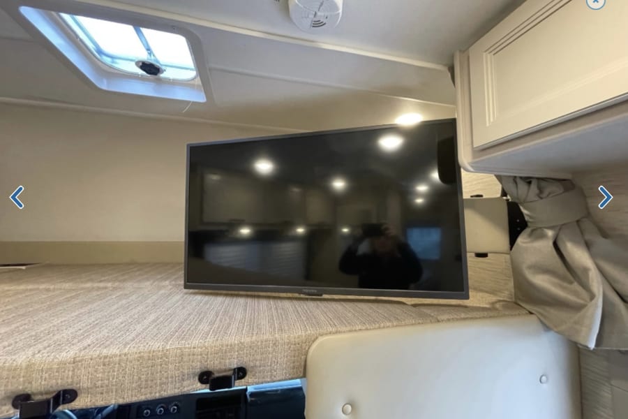 This **RV rental** interior features a cab-over bunk, mounted TV, and ceiling skylight, offering comfort for your journey.