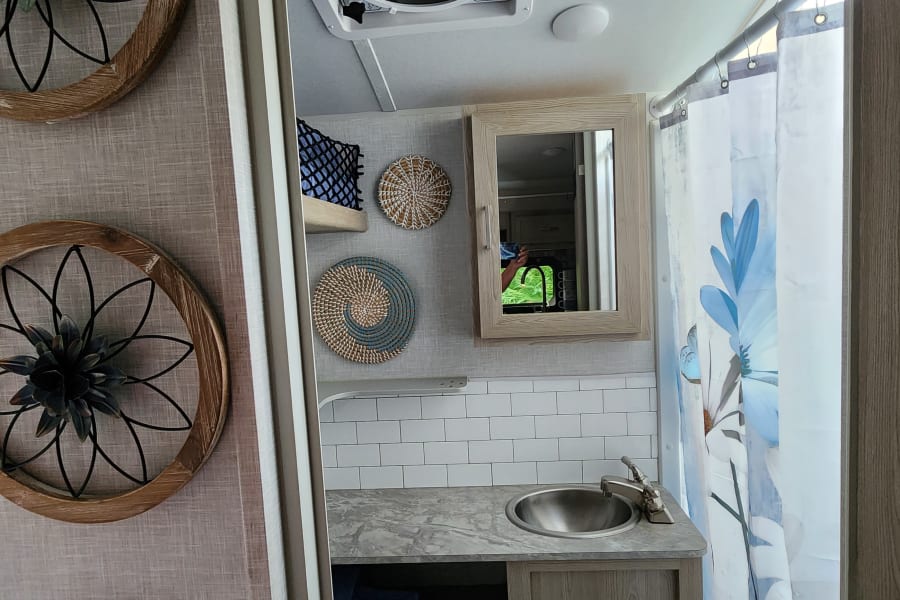 RV rental interior: A compact, modern bathroom with sink, subway tile backsplash, mirrored cabinet, and a blue floral shower curtain.