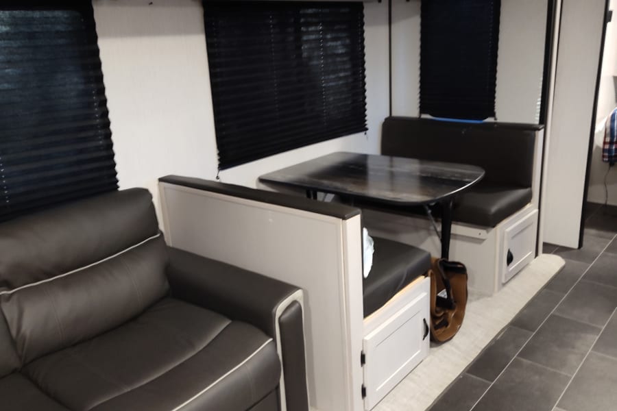 Modern RV rental interior: dark grey sofa, dinette with table & benches, sleek floor. A comfortable travel space.