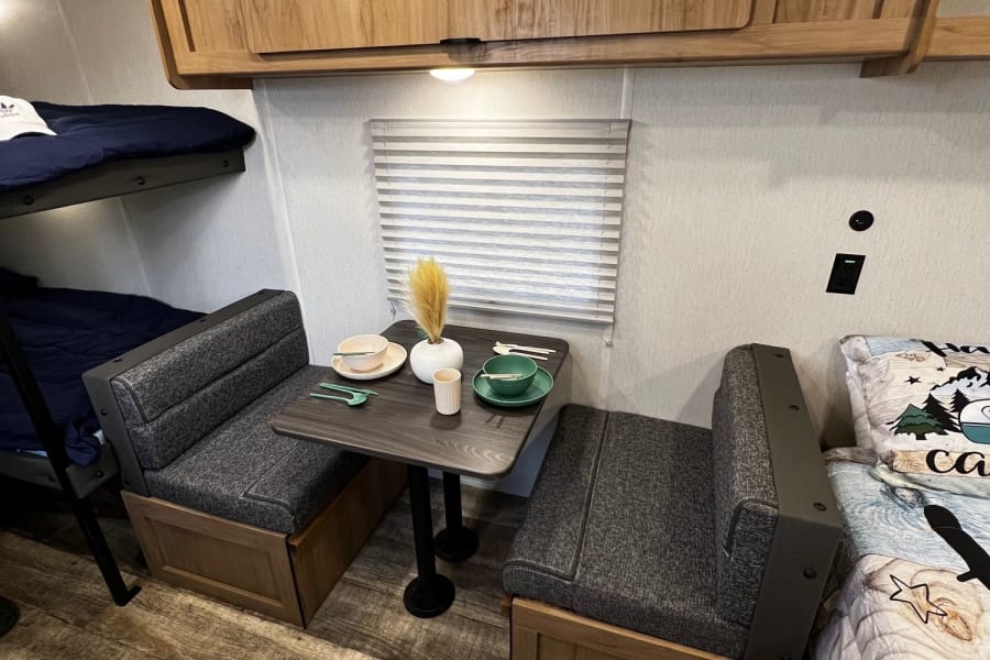 Cozy RV rental interior showing bunk beds, a dinette set with dishes, overhead cabinets, and wood flooring.