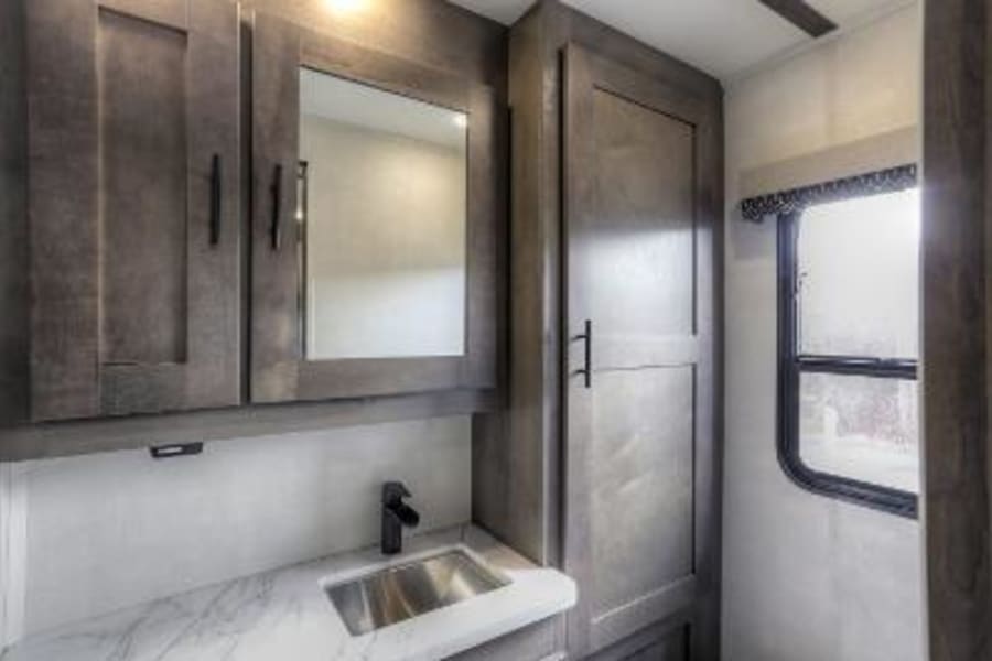 Modern RV rental bathroom featuring a vanity with sink, medicine cabinet, and ample storage, plus a window.