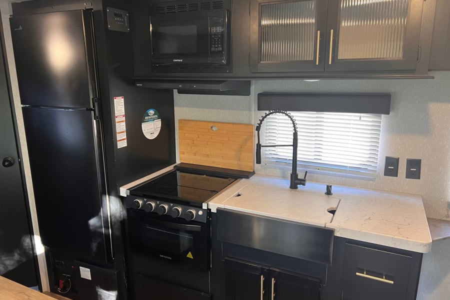 Modern RV rental kitchen featuring black appliances, light counters, and a large sink.