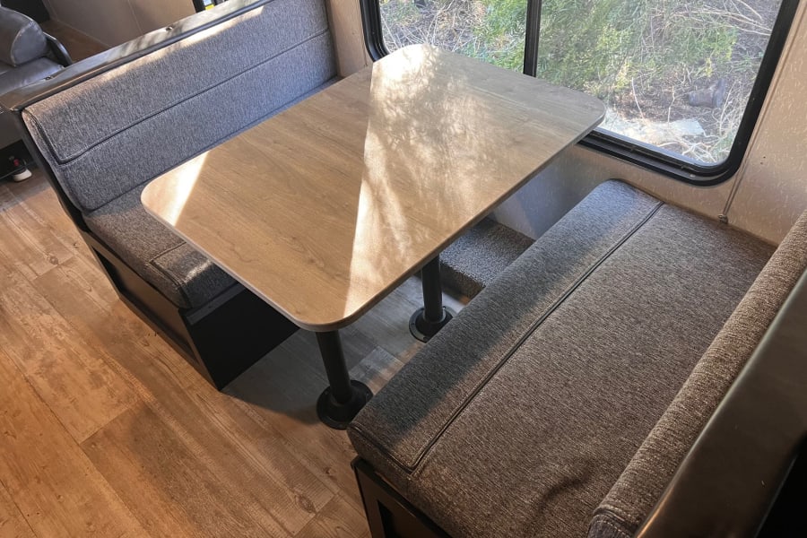 Cozy dinette in an RV rental with gray cushioned benches, a light wood table, and a sunlit window.