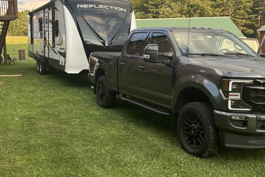 Powerful dark gray truck tows a large Reflection fifth-wheel RV. Ready for your next rv rental camping trip!