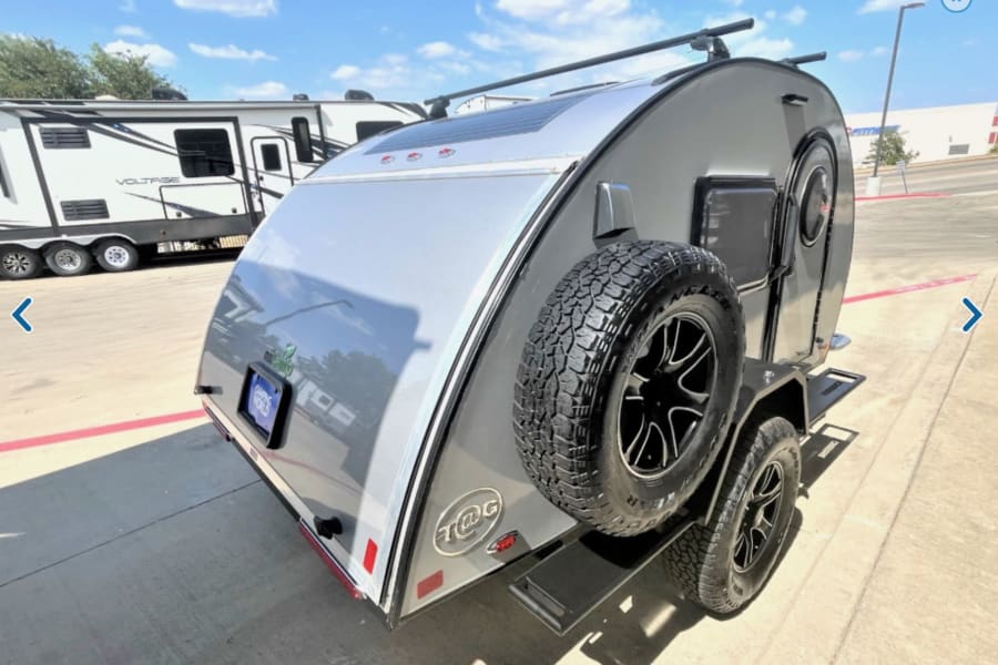 Explore off-grid adventures! This silver teardrop camper with a solar panel and spare tire is perfect for RV rental.