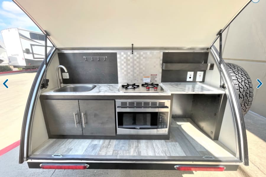 RV rental with a compact outdoor kitchen: sink, stove, microwave, storage, & counter space. Ready for adventures!