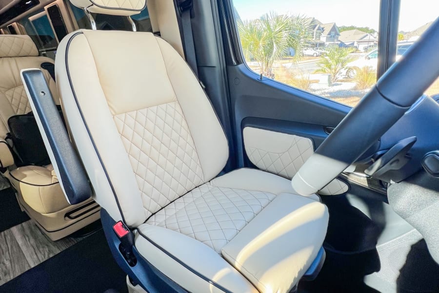 Luxury RV rental: Plush, quilted cream captain's seat with a clear view of palm trees & homes.