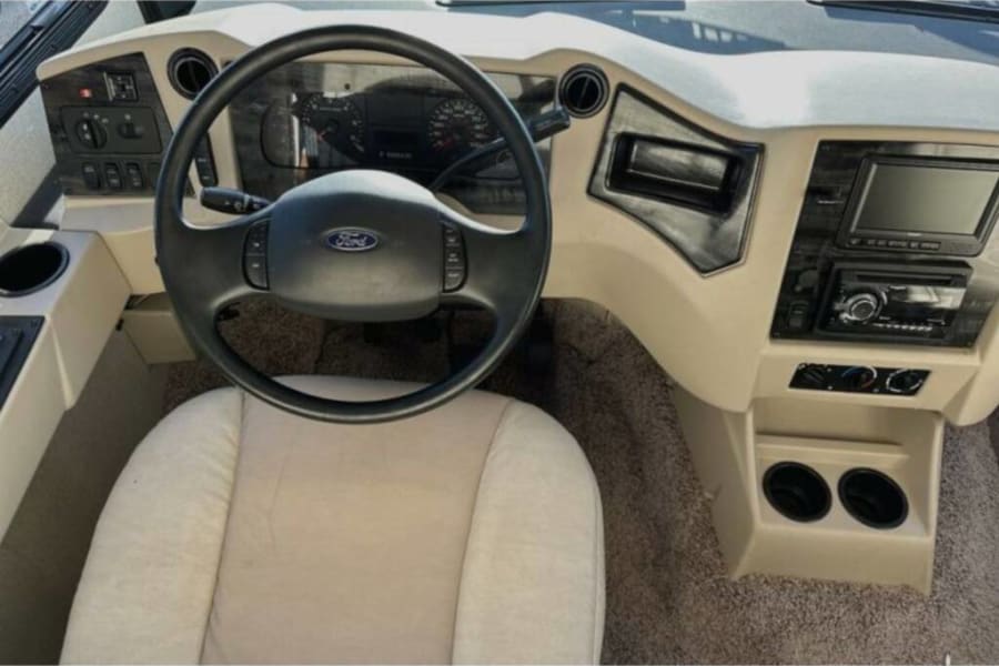 Spacious RV rental cockpit showing the Ford steering wheel, dashboard controls, infotainment system, and comfortable driver's seat.
