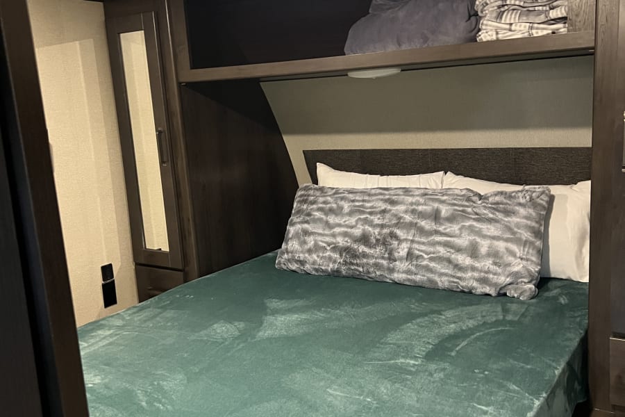 Cozy RV rental bedroom featuring a teal bedspread, overhead storage, and ceiling vent, providing a comfortable space.