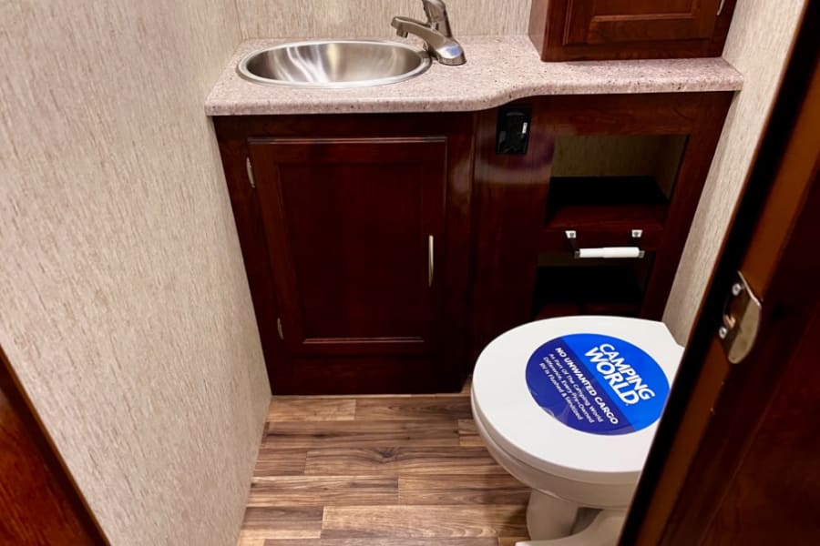 Compact RV rental bathroom features a sink, toilet, and storage, ready for your next adventure.