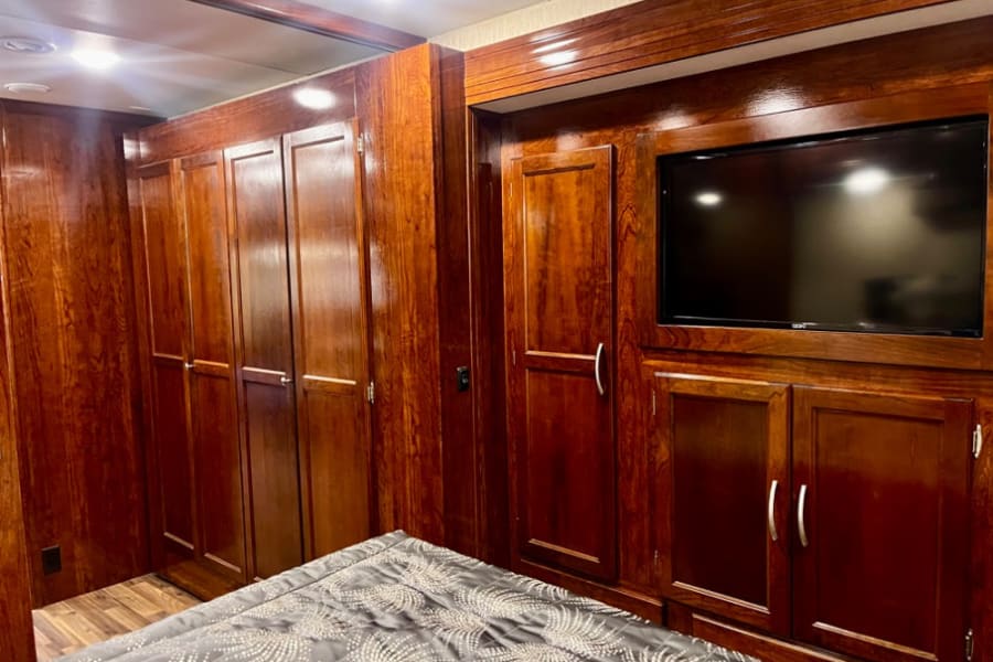 Spacious RV rental bedroom featuring rich wood cabinetry, a built-in TV, and ample storage. Perfect for travel.