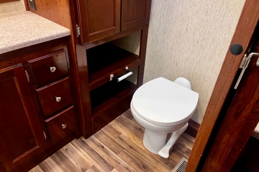 Inside an rv rental: a compact bathroom with a white toilet, wood vanity, and built-in storage shelves.