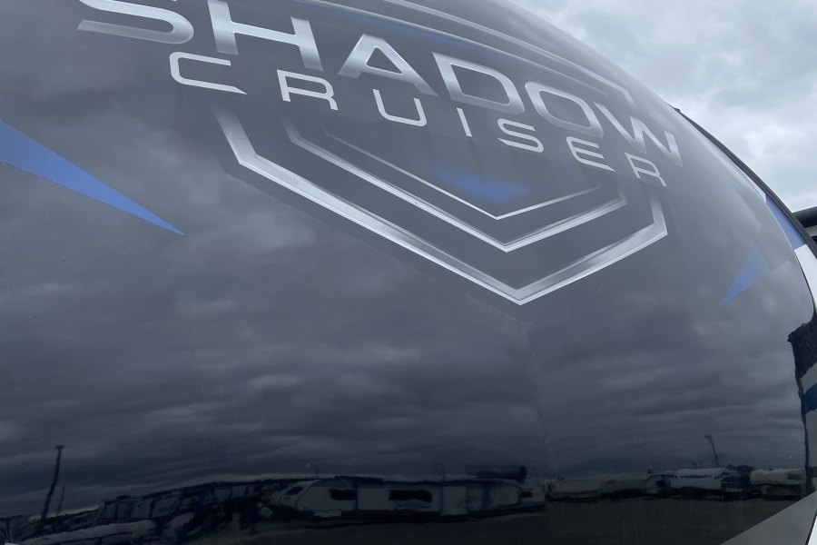 Close-up of a sleek black and white Shadow Cruiser RV's front, perfect for RV rental, reflecting cloudy skies.