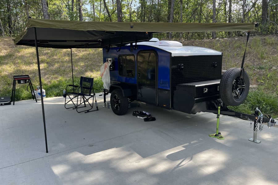 A compact blue camper trailer with a large awning parked on a paved campsite, ready for an RV rental outdoor adventure.