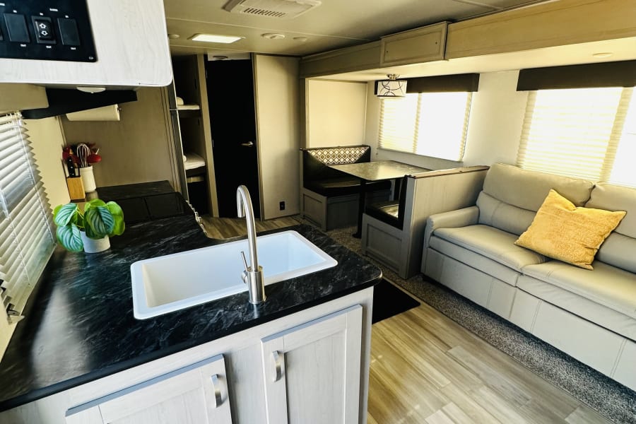 Spacious RV rental interior featuring a modern kitchen with sink, comfy light gray sofa, and dining booth. Ready for adventure!