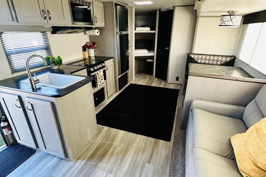 Explore this RV rental's bright interior, showcasing a modern kitchen, sofa, dining nook, and rear bunk beds.