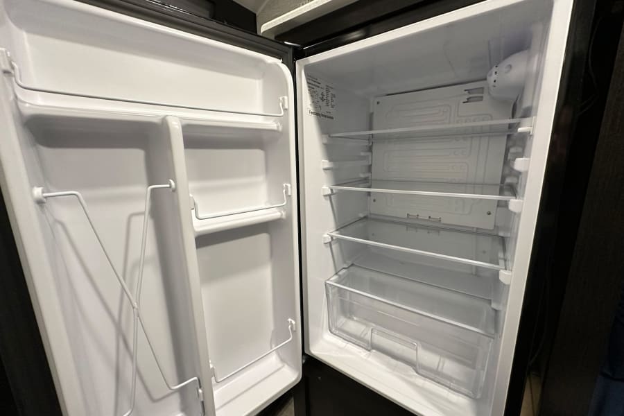 Empty RV rental refrigerator interior with clear shelves, wire door racks, and a crisper drawer, ready for your trip.