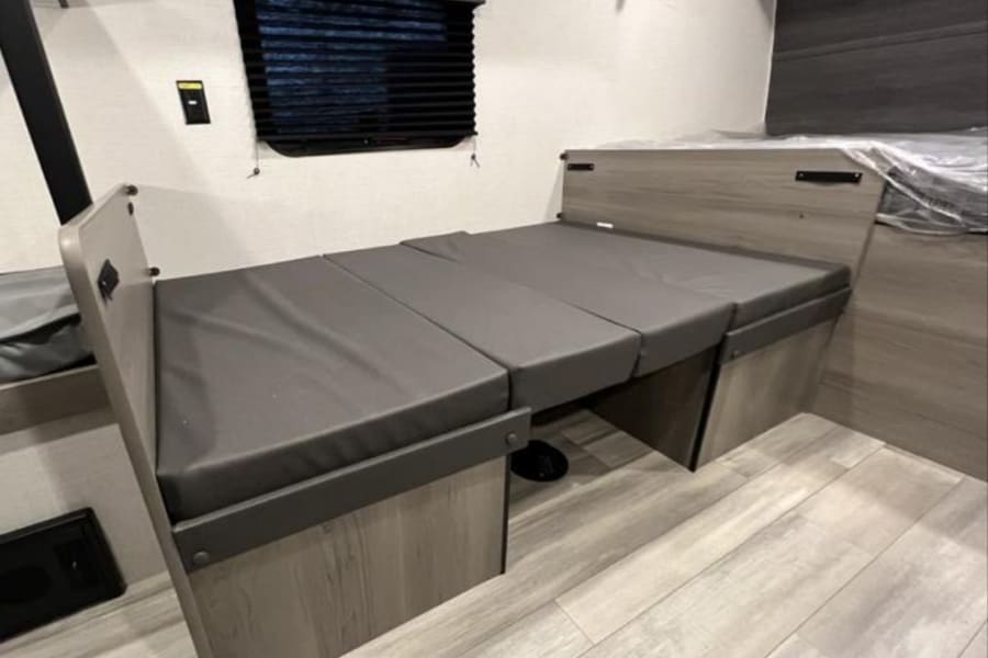RV rental interior showing a versatile dinette that converts into a bed, featuring sleek gray cushions and wood-look finishes.