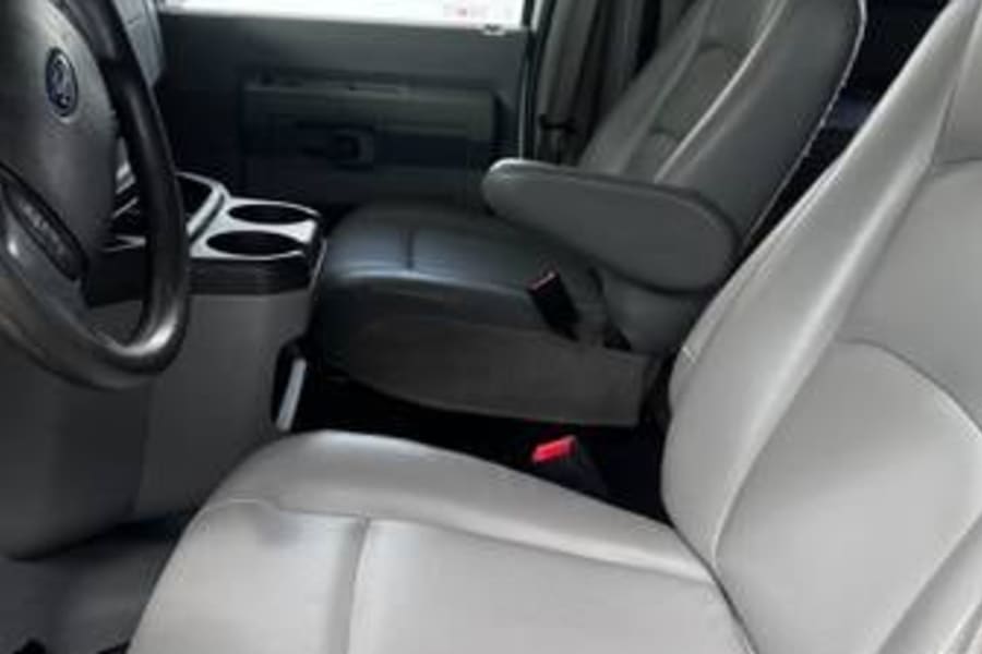 Light gray front seats and steering wheel of an RV rental van's interior, seen from the rear passenger area.