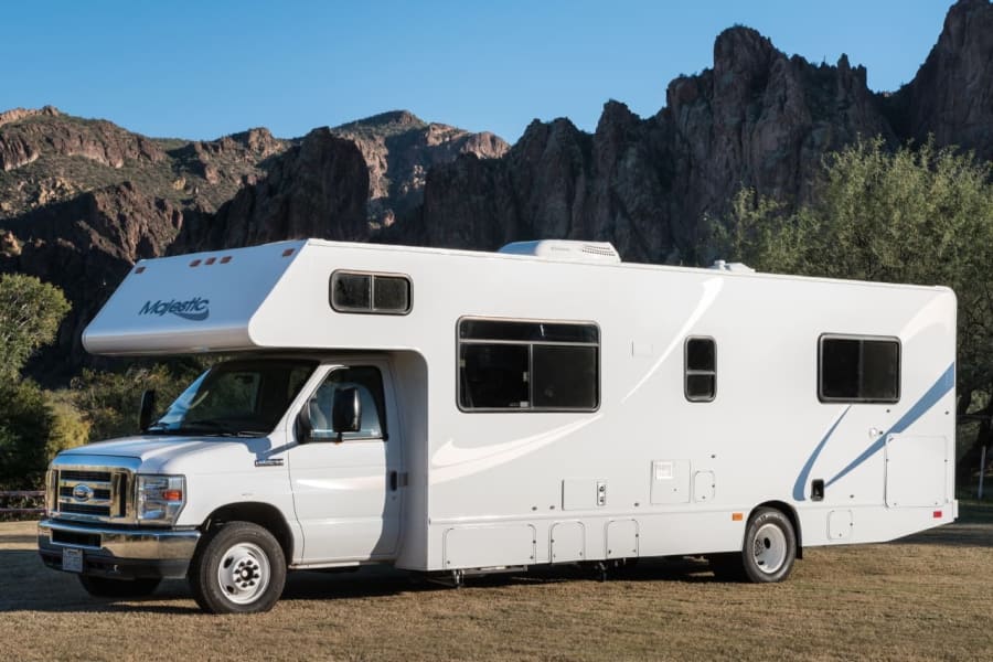 Majestic white RV rental on grass, set against rugged mountains. Ideal for scenic travel and adventure.