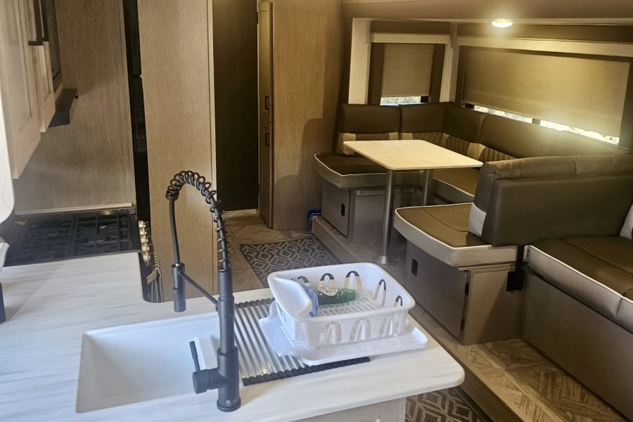 Spacious RV rental interior featuring a modern kitchen, compact stove, and comfortable U-shaped dinette.